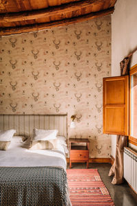 Interior of stylish bedroom with comfortable bed covered with coverlet near window decorated with curtains