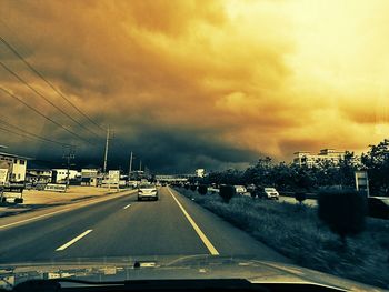 Cars moving on road against cloudy sky