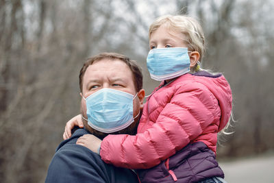 Father and daughter wearing flu mask looking away standing outdoors