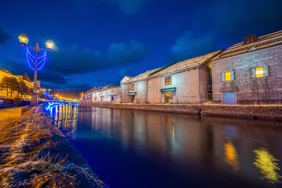 Illuminated buildings by lake against sky at night