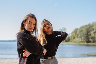 Portrait of young female friends standing at beach against sky