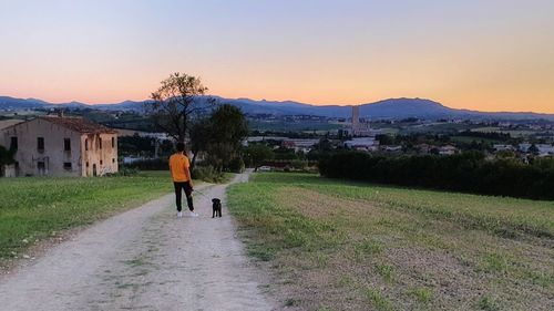 Rear view of man amidst buildings against sky during sunset