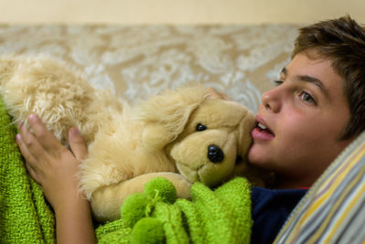 Boy with stuffed toy looking away while lying on sofa at home