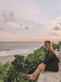 Woman sitting on beach by sea against sky