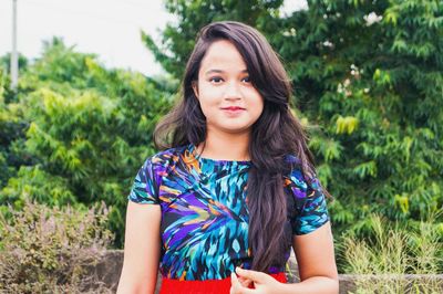 Portrait of young woman standing against trees