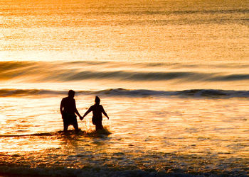 Romantic beach scene. couple holding hands walk in ocean with gentle waves at sunset. 