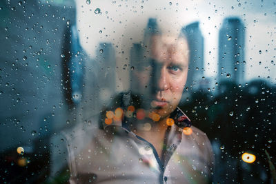 Portrait of man looking through wet glass window in rainy season