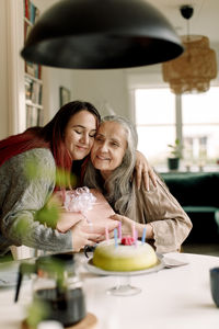 Smiling woman embracing mother and giving birthday present at home