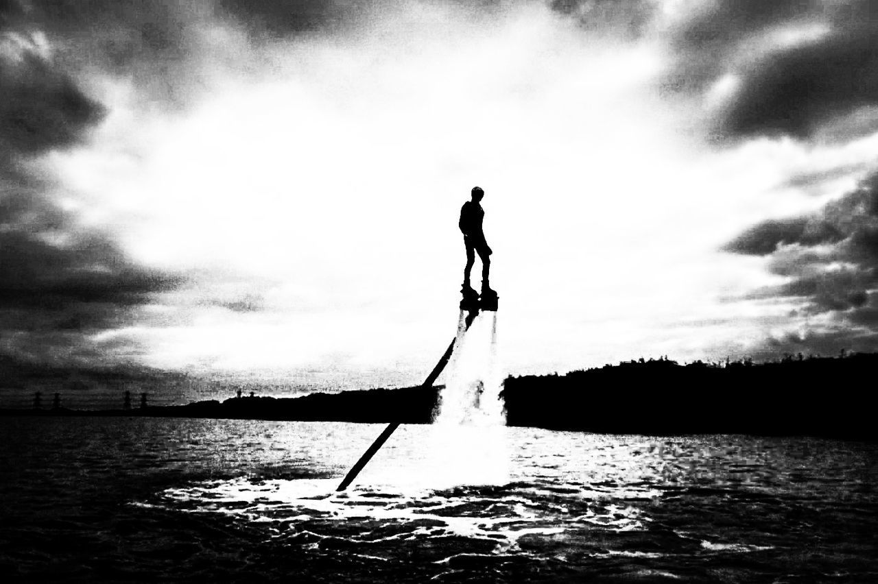 SILHOUETTE MAN STANDING IN WATER AGAINST SKY