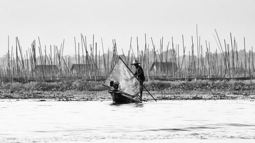 Fisherman standing on boat in lake against sky