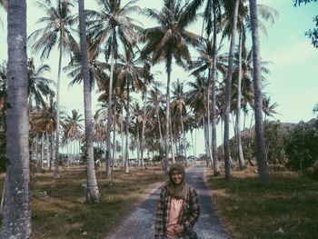 Portrait of smiling woman standing on road amidst coconut palm trees