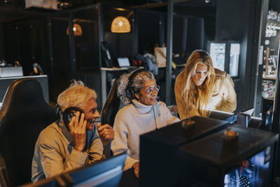 Woman helping senior couple playing computer game at gaming lounge during weekend