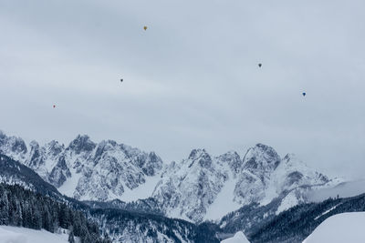 Scenic view of snowcapped mountains with hot air ballons in the distance against sky
