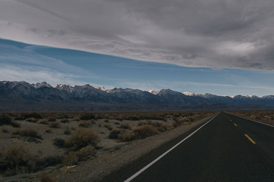 Empty road amidst landscape leading towards mountains against cloudy sky