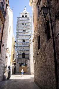 Rear view of people walking on alley amidst buildings in city