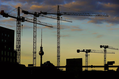 Silhouette cranes at construction site against sky during sunset