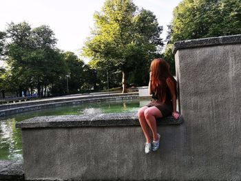 Rear view of woman sitting against trees against clear sky