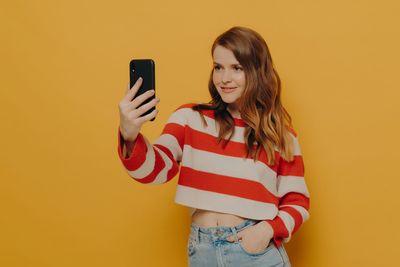 Young woman using mobile phone against yellow background