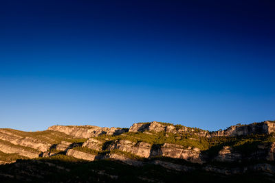 Low angle view of rocks against clear blue sky