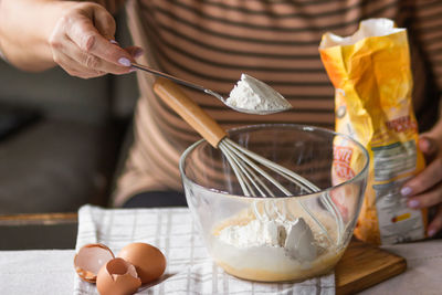 Senior woman adds a spoonful of flour to the dough in a glass bowl. ingredients for morning pancakes