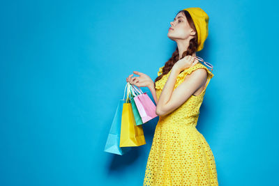 Young woman looking away while standing against blue background