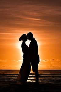 Silhouette couple embracing at beach against orange sky during sunset