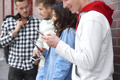 Young friends using smart phone while talking at city