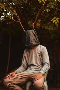 Midsection of man sitting by tree in forest