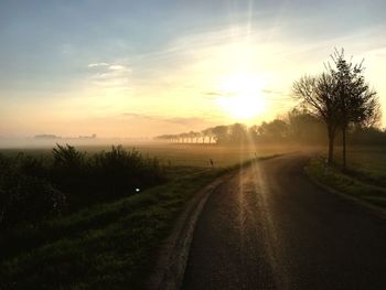 Road amidst field against sky during sunset