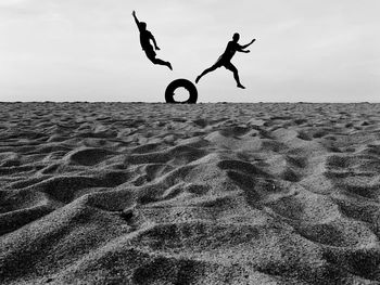 A silhouette of two males jumping at the sandy beach with strong figures 