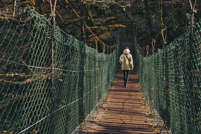 Rear view of woman walking on footbridge in forest