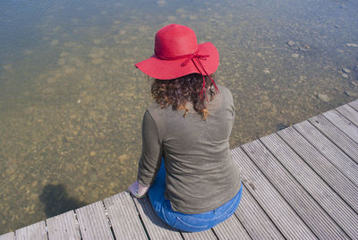 Rear view of woman sitting on pier over water