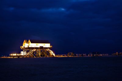 Illuminated building by sea against sky at night