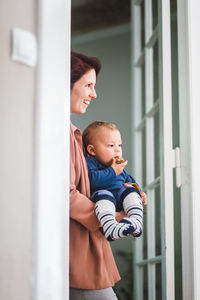 Smiling mother with son looking away while standing at home entrance