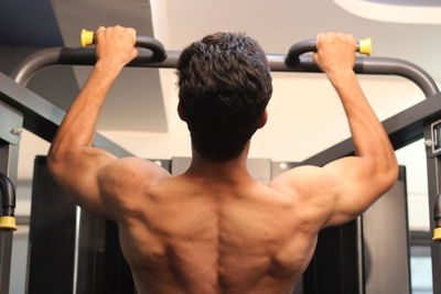 Rear view of shirtless man exercising in gym