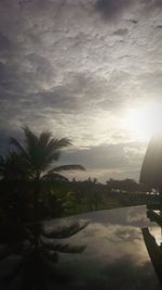 Palm trees by swimming pool against sky during sunset