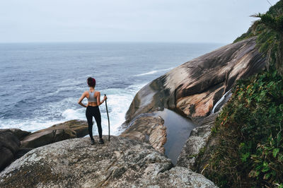 Rear view of woman standing on rock by sea