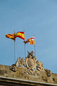 Low angle view of man holding flag against clear blue sky