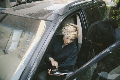 Female mechanic discussing with customer over digital tablet in car