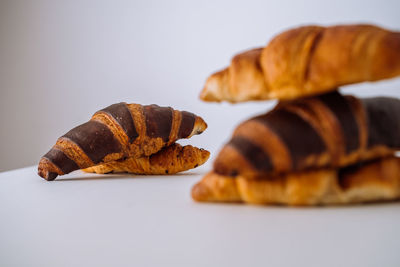 Bunch of delicious brown and chocolate croissants stacked on top of each other on a white table	
