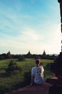 Rear view of man sitting on temple against sky