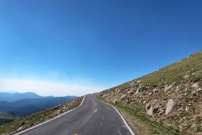 Road leading towards mountains against clear blue sky