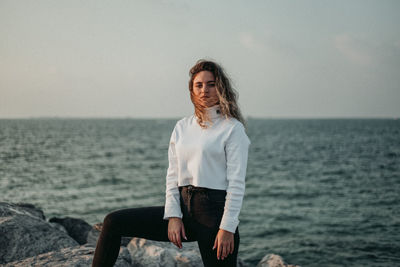 Woman sitting by sea against sky
