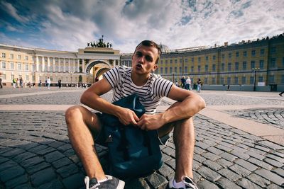 Young man sitting in city against sky