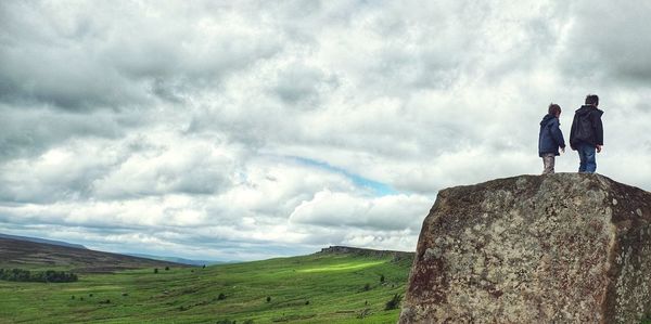 Two boys standing on landscape against cloudy sky