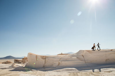 People on rock against sky on sunny day