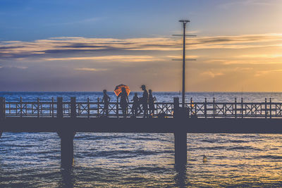 Silhouette people on pier over sea at sunset