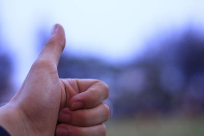 Close-up of human hand showing thumbs up against sky