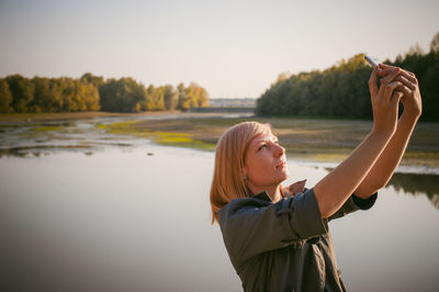 Woman photographing with mobile phone by lake