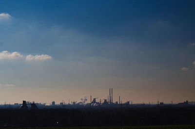 Silhouette of factory against sky at sunset